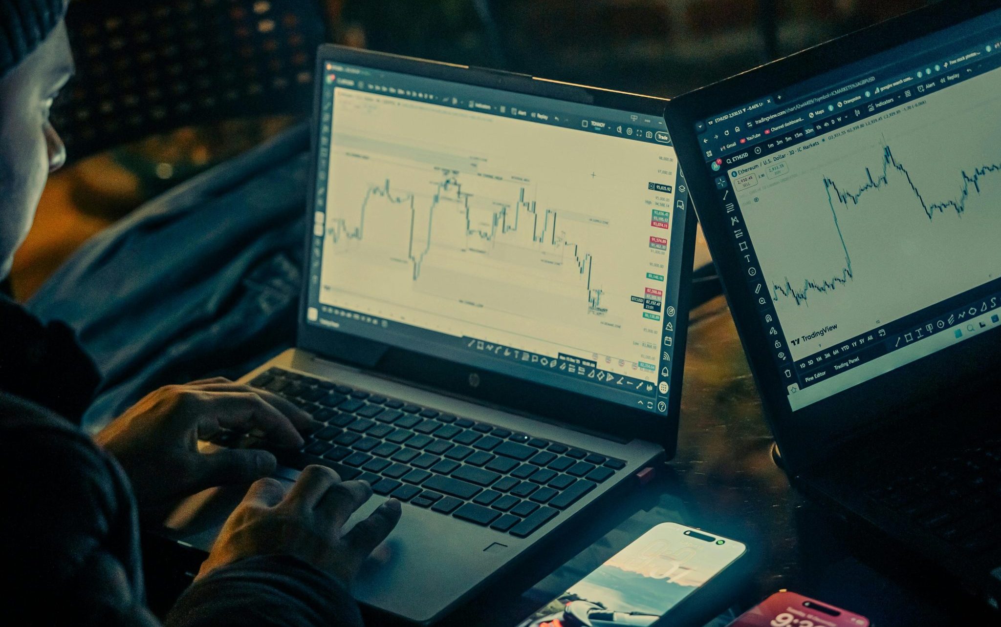 Person analyzing stock market data on laptops and smartphone outdoors at night.